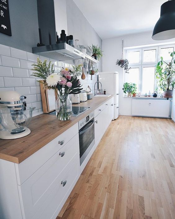 an airy Scandinavian kitchen with white cabinets and light stained wooden countertops that echo with the floors