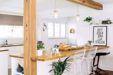 an airy modern white kitchen with light stained butcherblock countertops that match the wooden beam and pillar