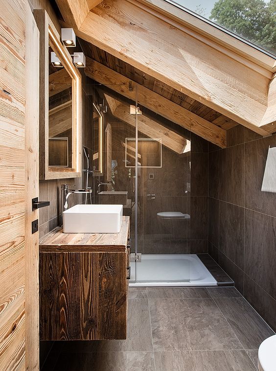 an attic chalet bathroom with a skylight, large scale tiles, a floating vanity, wooden beams and walls is amazing