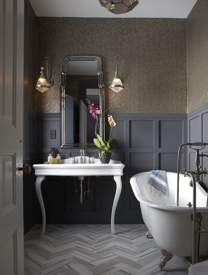 A chic moody bathroom with a vintage feel, a white free standing sink and a bathtub, a mirror, sconces and blooms