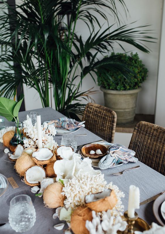 a coastal dinner tablescape with coconuts, corals and leaves plus candles is a very cool idea for a tropical space