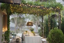 a dreamy Mediterranean dining space with greeneyr on the roof and potted greenery, wicker baskets and pendant lamps, wooden benches and a table