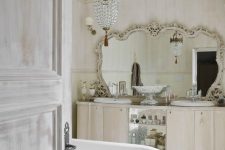a jaw-dropping vintage bathroom in neutrals, with a double vanity, a mirror in an ornated frame, a bathtub and a crystal chandelier