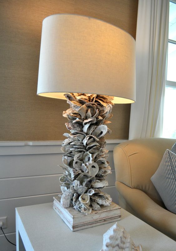 a large lamp with a neutral shade and lots of seashells covering the base looks very coastal and seaside