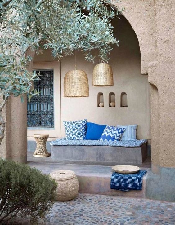A lively Mediterranean patio with a built in bench, blue upholstery, wicker pendant lamps, a side table and niches for storage