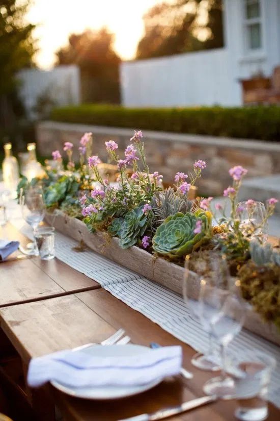 a long wooden planter with lots of succulents and some pink blooms is a chic and bold rustic centerpiece to rock