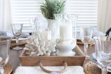 a lovely coastal farmhouse wedding centerpiece of a wooden tray, corals, candles in glasses with sand and some lavender is cool