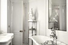 a refined and luxurious bathroom with white walls, a mosaic tile floor, a white vintage tub and an oversized mirror and a gold chandelier