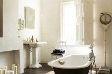 a refined vintage bathroom with a faux fireplace, a black clawfoot bathtub, a free-standing sink, a vintage chandelier and shutters on the window