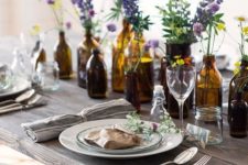 a summer table lined up with apothecary bottles and jars with bright blooms in them for a beautiful look