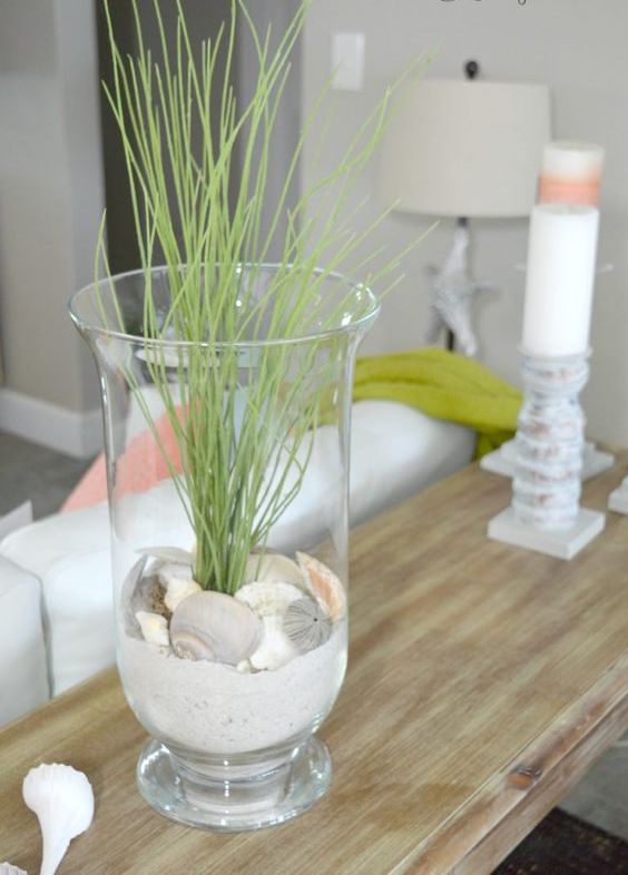 a tall glass with beach sand, seashells and some grass for decorating your console table