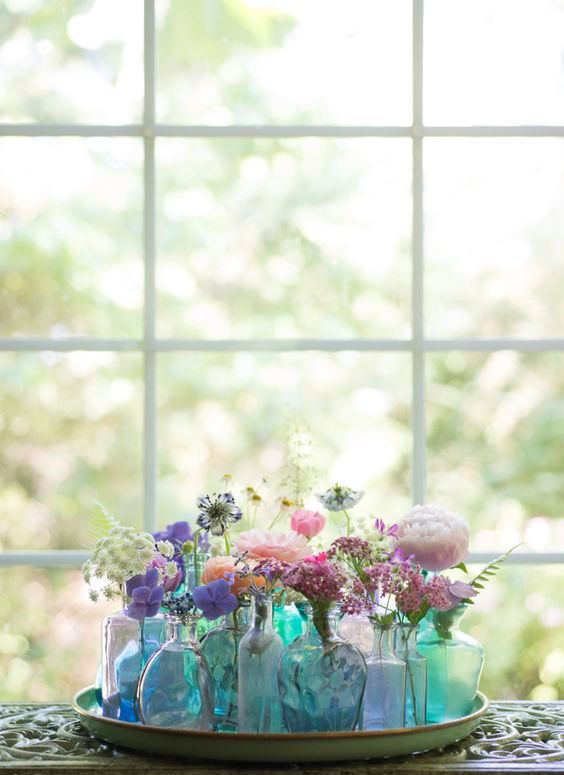 a tray with an arrangement of blue and green bottles and vases with colorful blooms
