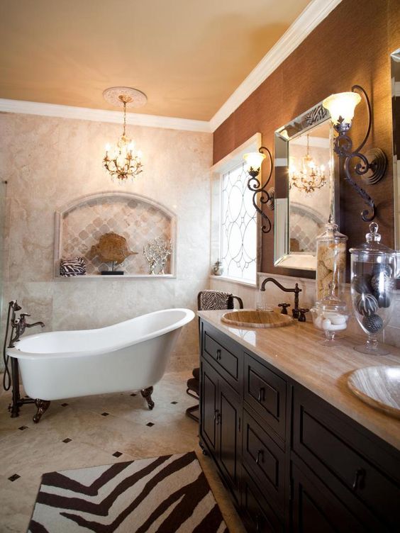 A vintage bathroom with marble and neutral tiles, a taupe wall, a dark stained vanity, a clawfoot bathtub and vintage lamps