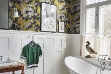 a vintage bathroom with moody floral wallpaper, creamy paneling, a free-standing bathtub, black and white tile floor and a vintage vanity