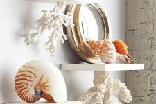 bathroom shelves with faux corals attached to them and with seashells and a mirror on them for giving a seaside feel to the space