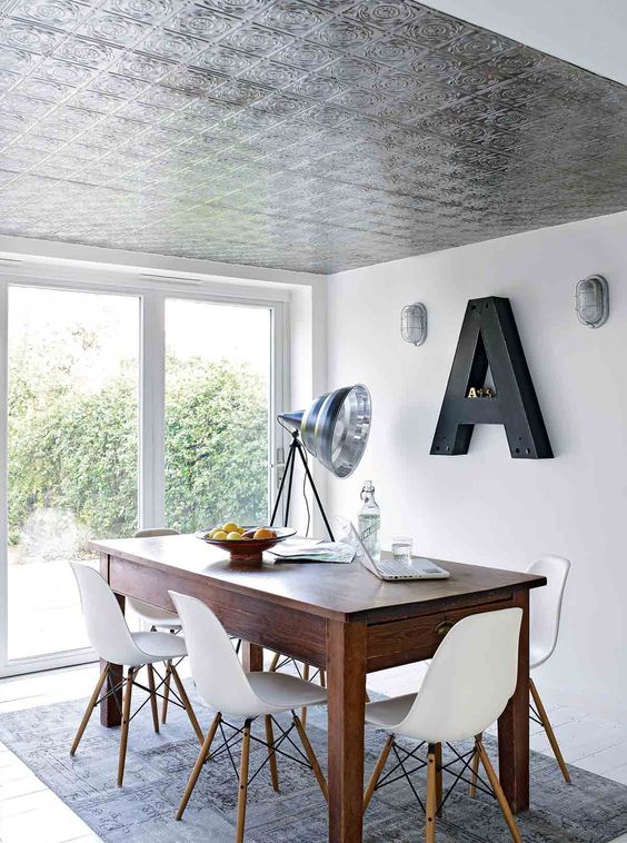 a Scandinavian dining space with a tin tile ceiling, a stained table and white chairs, a monogram and some lamps