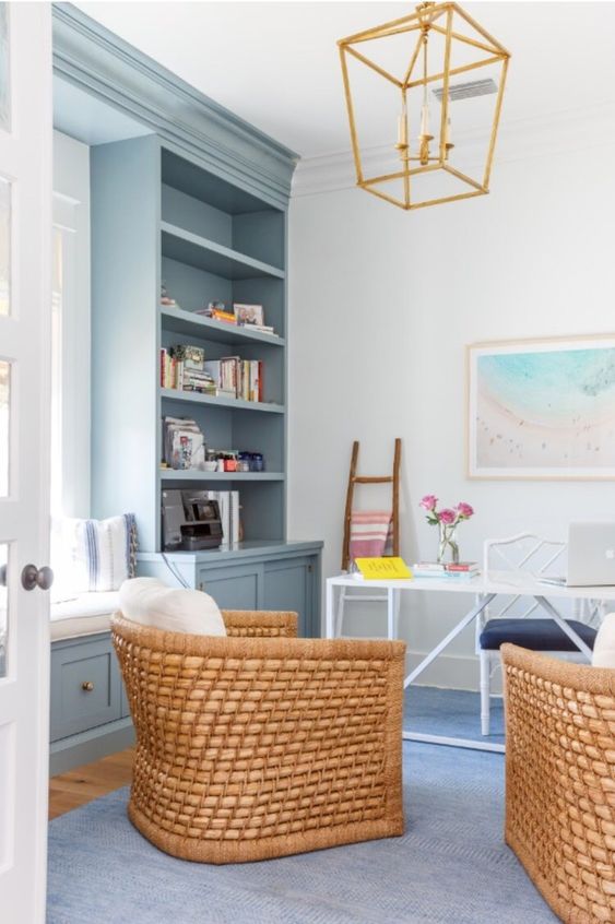 a beach home office with light blue storage units and a built-in daybed, an airy desk and rattan chairs and a gilded chandelier