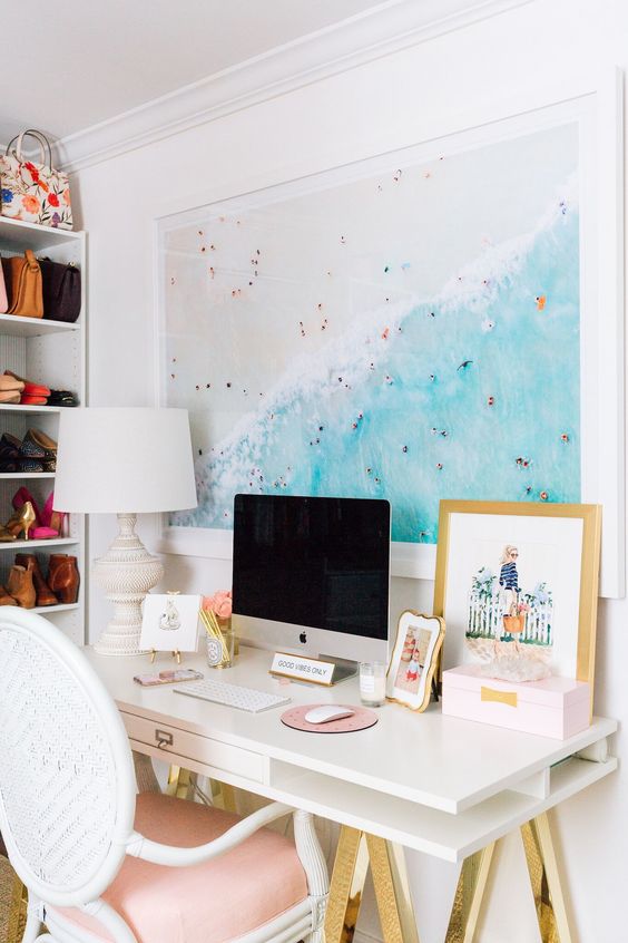 a beachy home office nook with a large beach photo, a white and gold desk, a pink chair and a chic table lamp is amazing