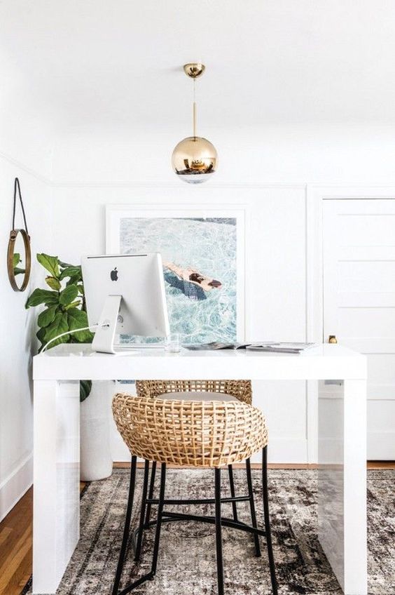 a beachy home office with a tall white desk, a couple of rattan stools, a beach photo and a statement potted plant