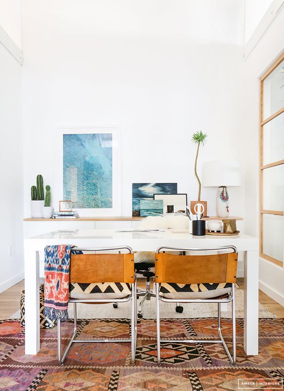 a boho coastal home office with a white desk, leather chairs, a white storage unit, sea-inspired artworks and potted plants