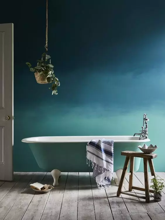 a bold bathroom with a catch gradient blue to green accent wall and a mint bathtub that matches it, with a potted plant