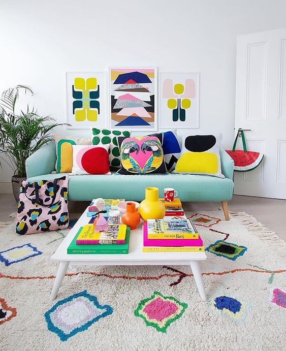 a bold summer living room with a colorful gallery wall, bright printed pillows and a rug plus bright books and vases