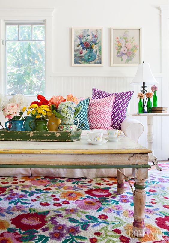 a bold summer living room with floral artworks, blooms in vases, printed pillows and a colorful floral rug for a cheerful feel