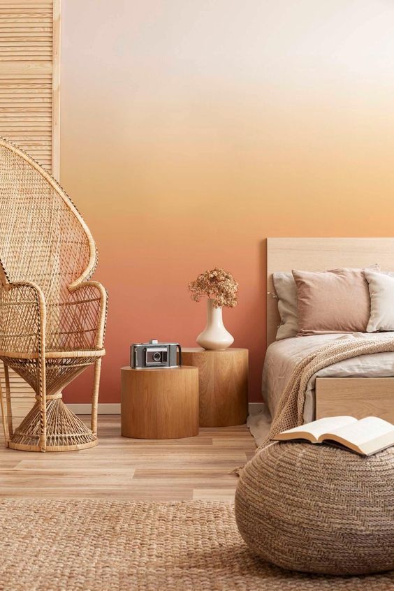 A bold warm colored bedroom with a gradient wall from neutral to rust, a bed with neutral bedding, tree stump nightstands, a papasan chair