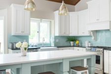 a bright beach kitchen with an aqua kitchen island and aqua tiles, white shaker cabinets, glass pendant lamps and vintage stools