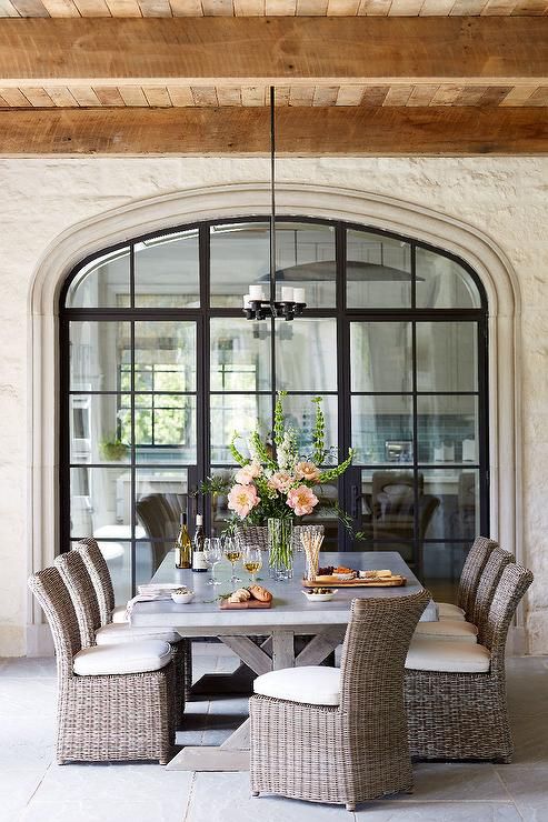 a classy farmhouse dining space with a large table with a concrete tabletop, wicker chairs with neutral upholstery and a chandelier