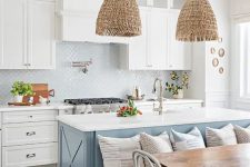 a coastal cottage kitchen with white shaker cabinets and a glossy tile backsplash, a blue kitchen island with a seating space and woven pendant lamps