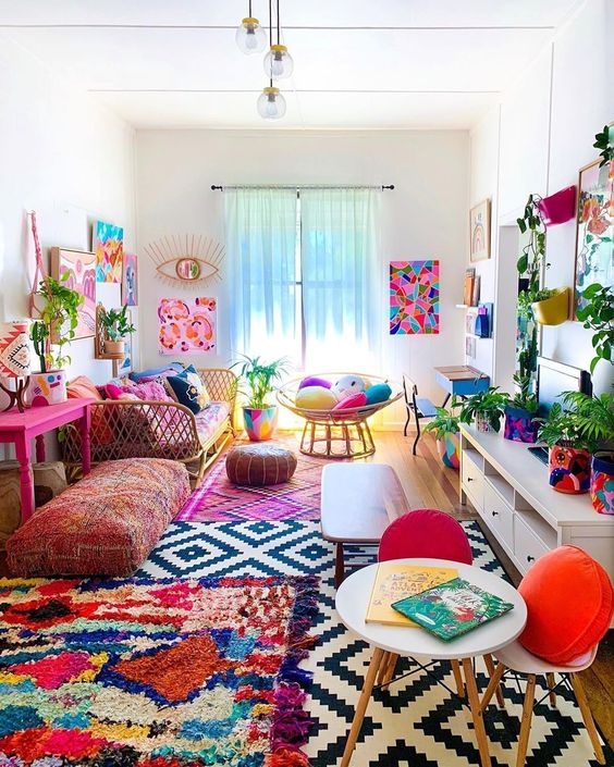 A colorful boho living room with a bright gallery wlal, colorful rugs and pillows, potted greenery and florals is summer like