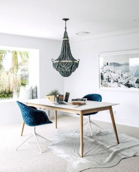 a fabulous coastal home office with a glazed wall, a desk, navy chairs, a wooden bead chandelier and a sea-inspired artwork