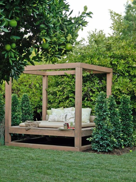a gorgeous garden outdoor bedroom with a solid wood bed with a frame and neutral upholstery and pillows placed right in the greenery