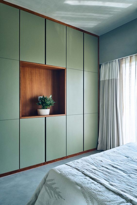 a green grey bedroom with grey walls and a floor, a sleek green storage unit with a niche for storage, a bed with neutral bedding