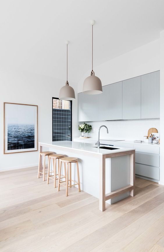 a minimalist beach kitchen with light blue ribbed cabinets and a white kitchen island, wooden stools and pretty pendant lamps