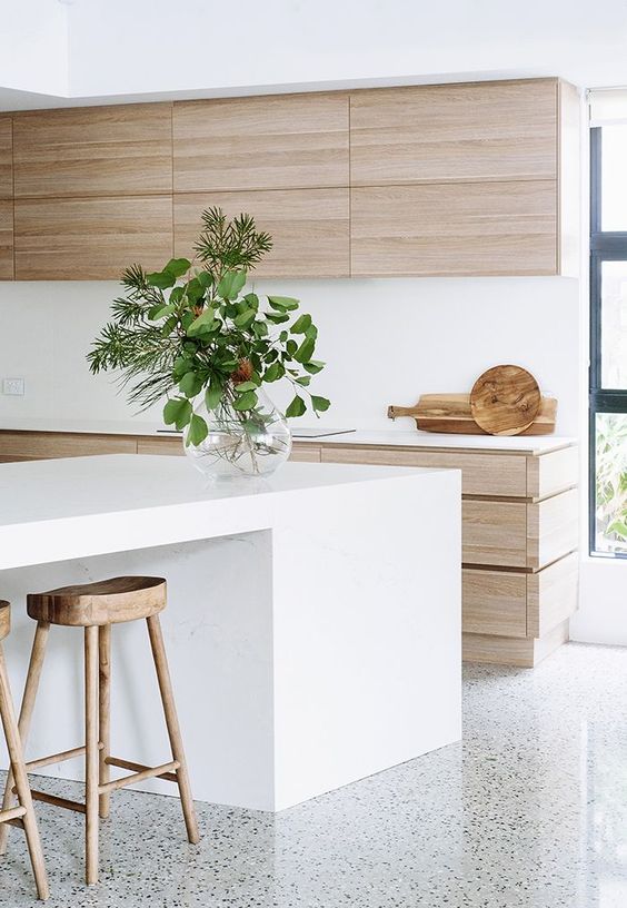A minimalist beach kitchen with light stained cabinets, a white backsplash, a large white kitchen island and light stained stools