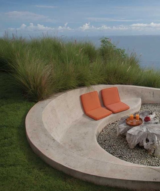 a minimalist outdoor space with a large seatign unit of white concrete, some cushions and a whitewashed wood coffee table