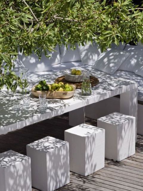 a minimalist terrace with a corner sofa with neutral upholstery, a white concrete table and matchign stools
