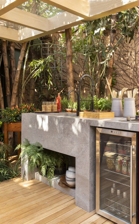 A modern kitchen of concrete with a built in sink, a fridge and roof over the space is a great nook to cook something delicious