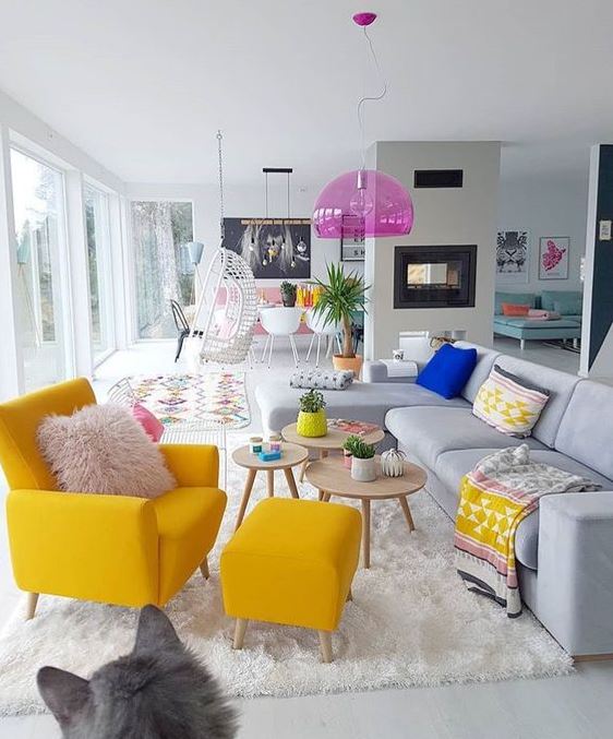 a neutral living room with a bright yellow chair, boho textiles, a pink pendant lamp and potted plants