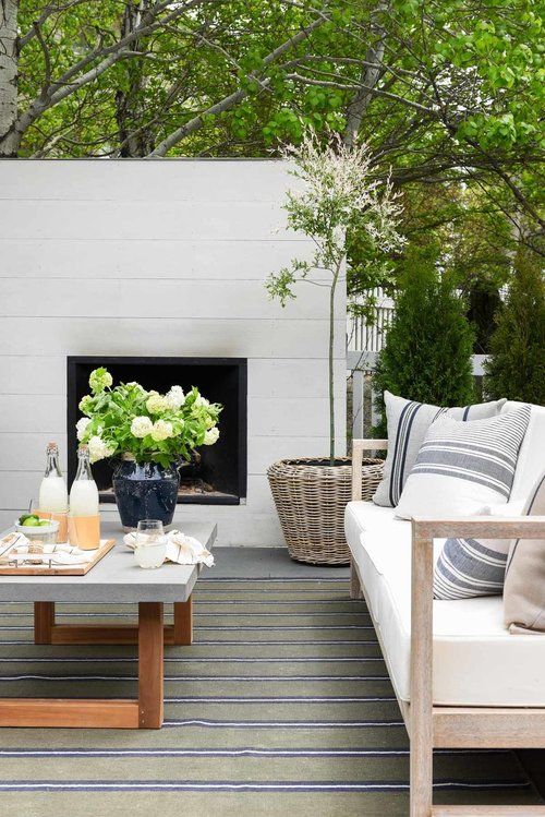 A neutral modern outdoor living room with a fireplace, a concrete coffee table, a light stained sofa with neutral upholstery