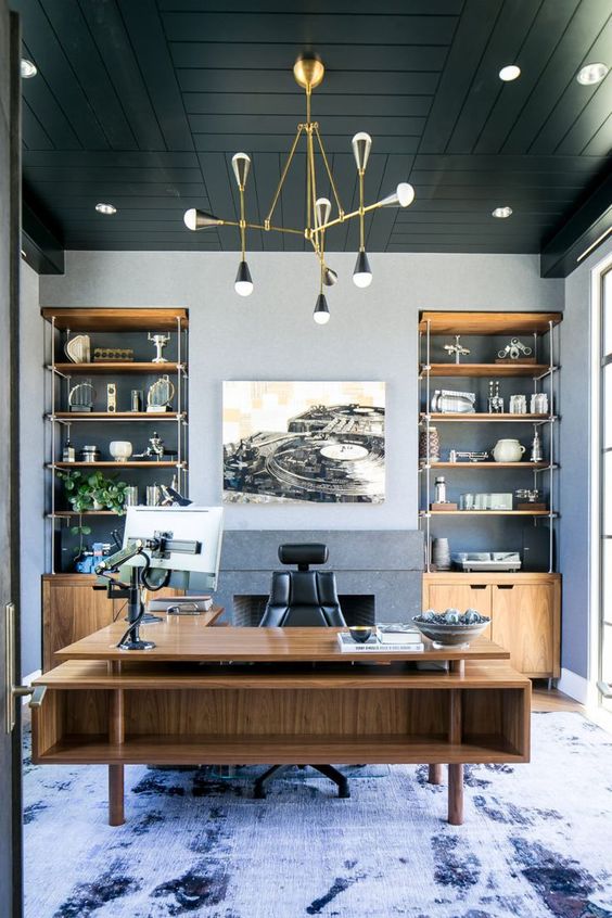 A refined beach home office with grey walls, a black wooden ceiling, built in storage units and a large stained desk plus a sea inspired rug