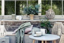 a relaxed outdoor space with a concrete daybed with pillows, a concrete side table and a coffee table, some lanterns and greenery