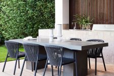 a sleek and elegant outdoor dining space with a metal and concrete table and metal black chairs plus candles and greenery