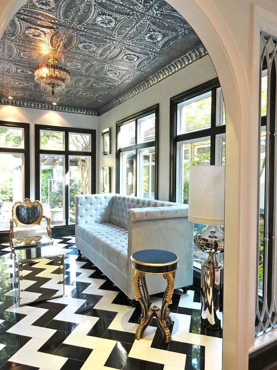 a sophisticated space with a series of windows, an elegant sofa, black and gold chairs and a lovely tin tile ceiling