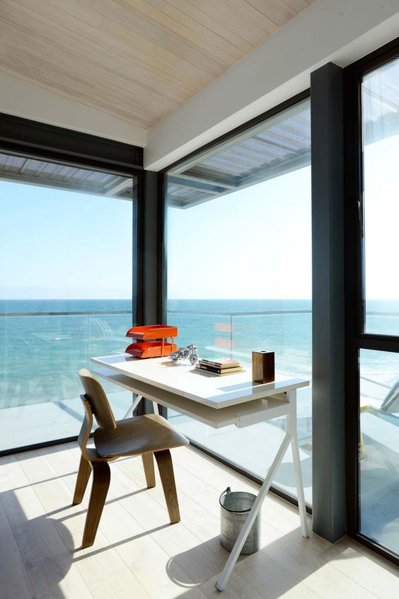 a stunning modern beach home office with glass walls, a sleek white desk and a stained chair and gorgeous sea views