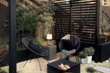 a stylish modern outdoor living room with black round chairs, a fire pit with firewood, a concrete side table and lots of greenery