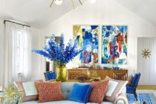 a super bold living space with bright artworks, blooms, a blue printed rug, printed pillows is a fun and bold summer space