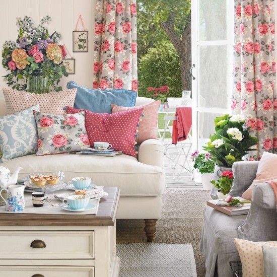 A vintage inspired living room with florla curtains, printed pillows, potted blooms and greenery and bright blankets for summer